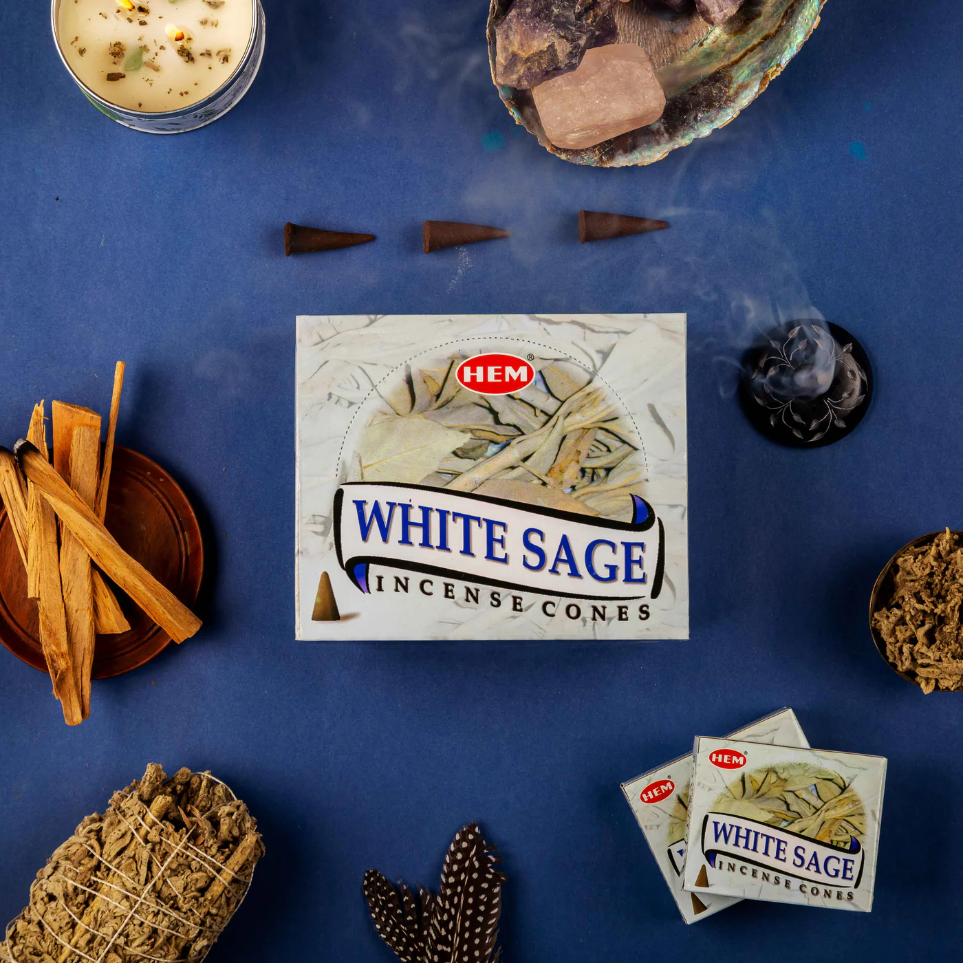 HEM White Sage Incense Cones packaging surrounded by incense sticks and smoke on a blue background
